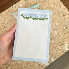 a hand holding a piece of paper with blue flowers on it and lined notes attached to the side