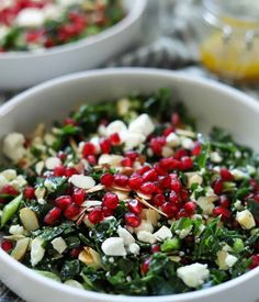 two white bowls filled with greens and pomegranates on top of a table