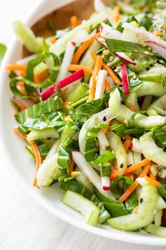 a salad with carrots, celery and radishes in a white bowl