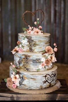 a three tiered cake decorated with flowers and heart shaped topper on a wooden table