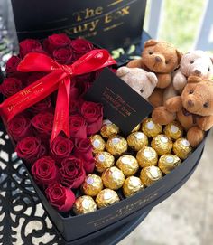 two teddy bears sitting on top of a black box filled with roses and chocolates