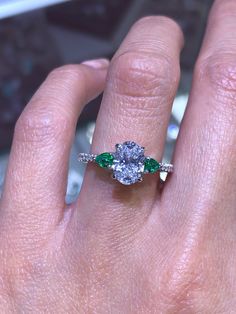 a woman's hand with a diamond and emerald engagement ring on her left hand