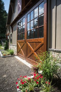 a large wooden garage door sitting next to a lush green field with red flowers in the foreground