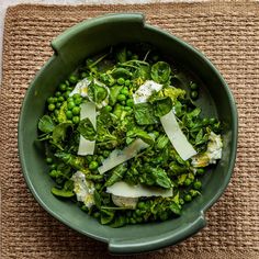 a bowl filled with peas and cheese on top of a place mat next to a spoon