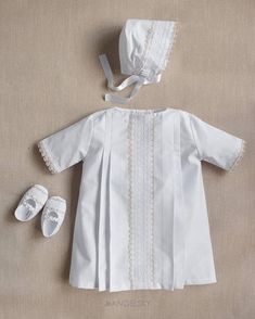 a baby's christ gown and shoes are laid out on the floor