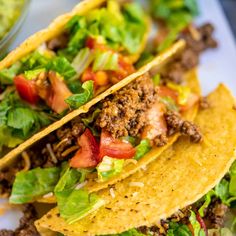 three tacos with meat, lettuce and tomatoes on them sitting on a plate