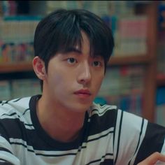 a young man sitting at a table in front of a bookshelf