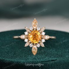 a ring with an orange diamond surrounded by white and yellow diamonds on a green velvet box