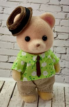 a small teddy bear wearing a green shirt and brown tie with a hat on its head