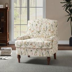 a chair sitting in front of a window next to a book shelf and potted plant