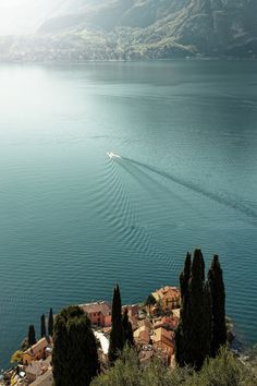 a boat traveling across a large body of water next to trees and mountains in the background