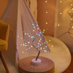 a small tree with multicolored lights on it in a room next to a chair