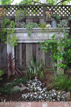 an outdoor fireplace surrounded by greenery and brick pavers in front of a wooden fence