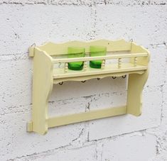 a yellow shelf with two green cups on it against a white brick wall in the daytime