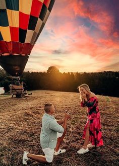 a man kneeling down next to a woman in front of a hot air balloon at sunset