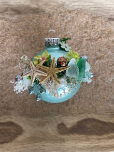 a christmas ornament with starfish, shells and seaweed in it on a wooden surface