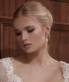 a woman in a wedding dress looking down at her hand on her shoulder and wearing earrings