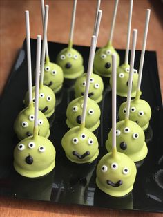 green cake pops with googly eyes and white sticks sticking out of them on a black plate