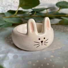 a small ceramic bunny rabbit ring on a white tablecloth next to some green leaves