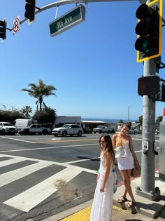 two women are standing on the sidewalk at an intersection with traffic lights and street signs