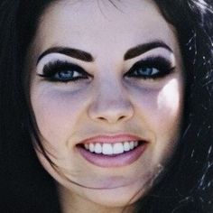 a woman with black hair and blue eyes smiles at the camera while wearing white makeup