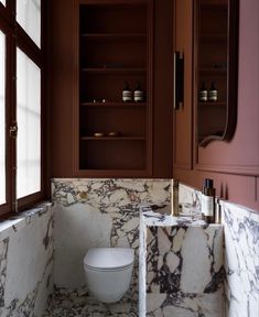 a white toilet sitting inside of a bathroom next to a sink and cabinets in a room