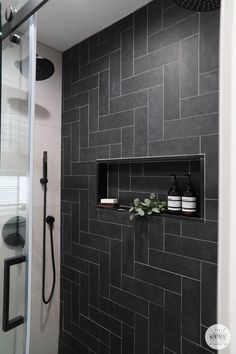 a black tiled shower with shelves on the wall and plants in vases next to it