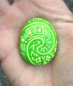 a hand holding a green and yellow painted rock