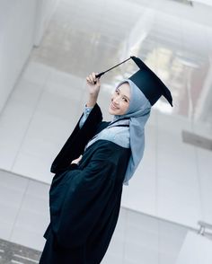 a woman wearing a graduation gown and holding a black hat on top of her head