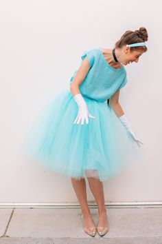 a woman in a blue dress and white gloves is leaning against a wall with her hands on her hips