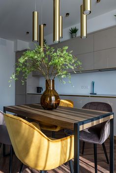 a dining room table with yellow chairs and a brown vase filled with green plants on it