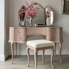 a pink vanity with mirror, stool and flowers