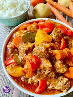 a white bowl filled with meat and veggies next to carrots, potatoes and rice