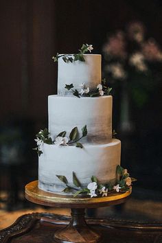 a three tiered cake with white flowers and greenery on the top is sitting on a table