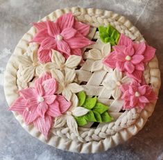 a cake decorated with pink and green flowers on top of a white pie crust covered in icing