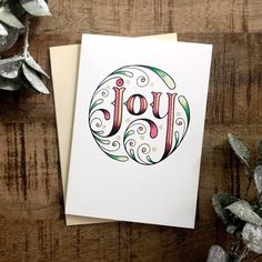 a card with the word joy on it next to some silver foil and greenery