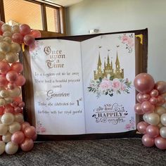 an open book decorated with balloons in the shape of castle and flowers, sitting on top of a table