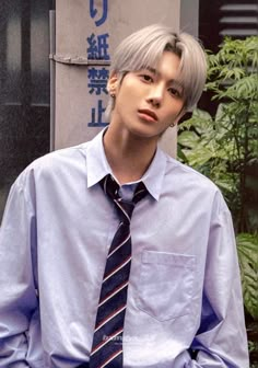 a man with grey hair wearing a blue shirt and tie standing in front of a building