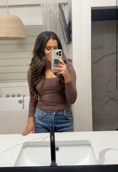 a woman taking a selfie in front of a bathroom sink and mirror with her cell phone