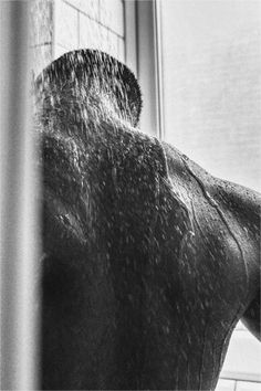 a man standing in front of a window with his back turned to the camera while it rains