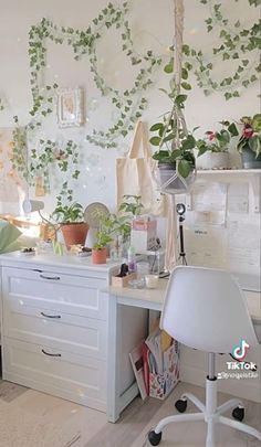 a white desk topped with lots of plants and office supplies next to a wall mounted planter