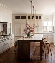 a large kitchen with white cabinets and wooden floors is pictured in this image, there are stools at the center of the island