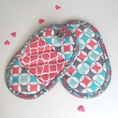 two oven mitts sitting on top of a white table covered in pink and blue hearts