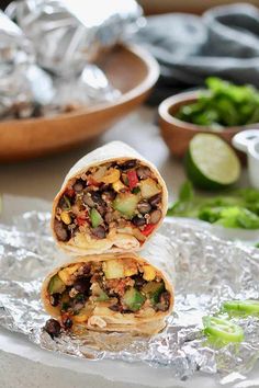 two burritos are stacked on top of each other in tin foil with vegetables