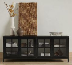 a black entertainment center with glass doors and vases on the top, in front of a white wall