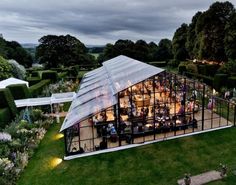 an aerial view of a glass house in the middle of a lush green field with lots of trees