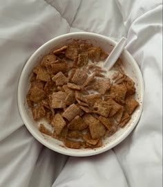 a bowl of cereal is sitting on a bed with white sheets and a spoon in it