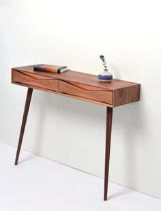 a wooden table with two drawers and a vase on top, against a white wall