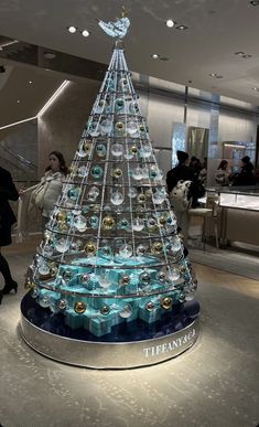 a christmas tree made out of glass bottles in a lobby with people standing around it