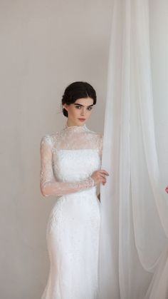 a woman in a white wedding dress standing next to a curtain with her hands on her hips